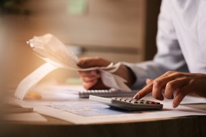 Eine Person überprüft Belege und tippt auf einem Taschenrechner, während verschiedene Dokumente auf dem Schreibtisch liegen – ein typisches Szenario bei der Einhaltung neuer Steuervorschriften für Selbstständige und Freiberufler.