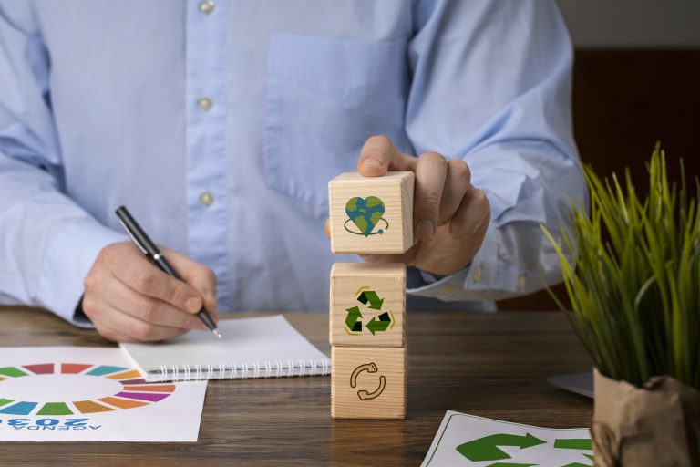 Ein Mann stapelt Holzwürfel mit Recycling- und Umweltsymbolen neben einem Notizblock mit der Agenda 2030 – ein Symbol für nachhaltige Investitionen und strategische Planung im grünen Markt.