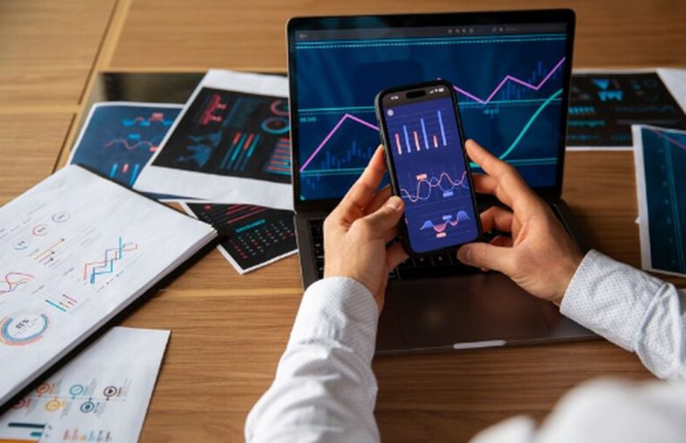 Eine Person analysiert Finanzdaten auf einem Smartphone und Laptop, umgeben von Diagrammen und Berichten – Symbolbild für moderne Anlagestrategien mit digitalen Tools und die Nutzung von ETFs zur Portfolio-Diversifikation.
