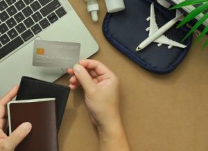 Eine Person hält eine Kreditkarte in der Hand, während sie einen Reisepass und ein Portemonnaie vor einem Laptop und Reisezubehör auf einem Tisch vorbereitet – Symbolbild für die Nutzung von Kreditkarten bei Auslandsreisen.