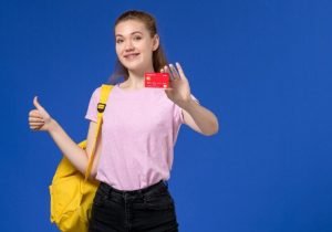 Eine junge Studentin mit Rucksack zeigt lächelnd eine Kreditkarte und hebt den Daumen hoch – Symbolbild für Kreditkarten für Studenten und den Einstieg in die finanzielle Selbstständigkeit.