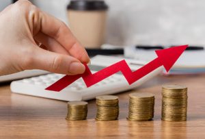 Eine Hand hält einen roten Pfeil, der über aufgestapelten Münzen nach oben zeigt – Symbolbild für finanzielles Wachstum und die Auswirkungen der Politik der Zinssätze in Deutschland auf Investitionen und Sparverhalten.