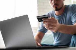 Mann, der mit seinem Laptop eine Online-Zahlung per Kreditkarte tätigt, Symbol für digitale Einkäufe und finanzielle Sicherheit.