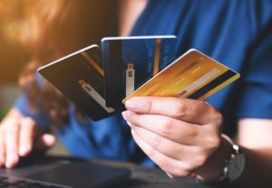 Frau hält mehrere Kreditkarten in der Hand vor einem Laptop, Symbol für die Nutzung verschiedener karten im Online-Zahlungsverkehr.